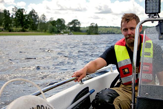 En person i flytväst sitter i en motorbåt och tittar in i kameran.