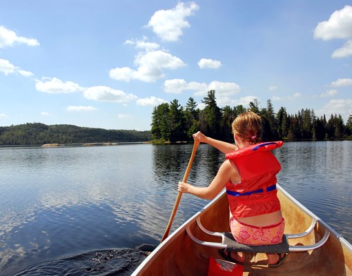 Foto på barn med röd flytväst som paddlar kanot på en sjö 