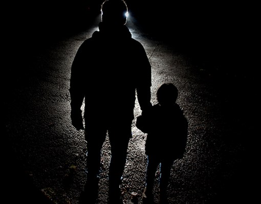 Foto på konturerna av en vuxen och ett barn i mörker belysta av billyktor