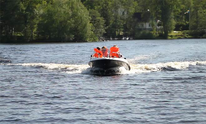En motorbåt på en sjö sommartid med fyra personer i orange flytväst.