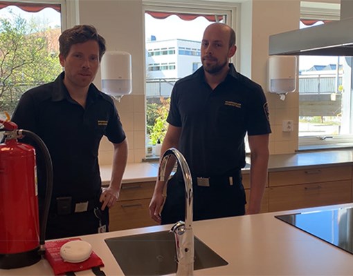Foto på två brandingenjörer i ett kök som pratar om brandskydd i hemmet