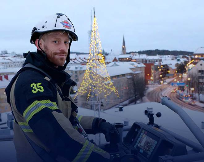 En person iklädd larmställ står i en räddningskorg högt över mark.