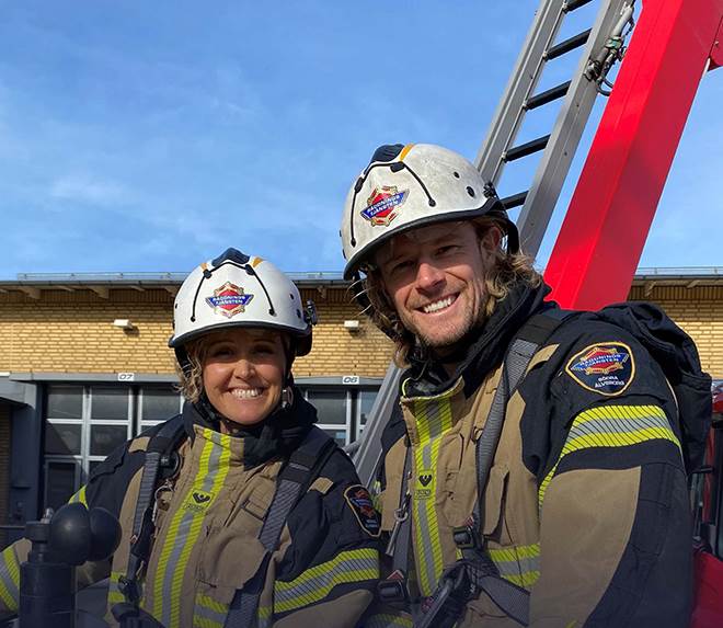 Två brandmän står i en räddningskorg på ett höjdfordon och ler.